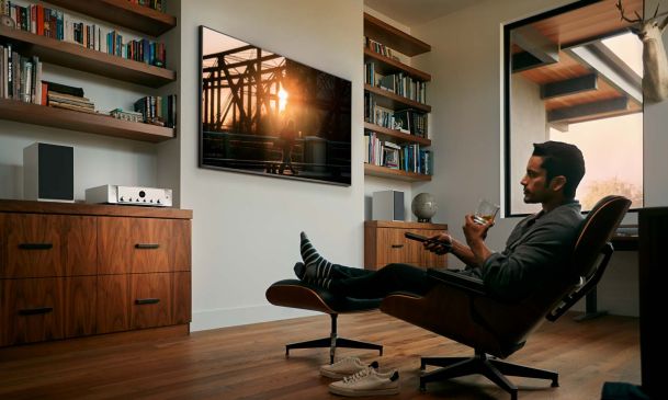 Man with a drink in a chair watching tv and listening to marantz high performance audio